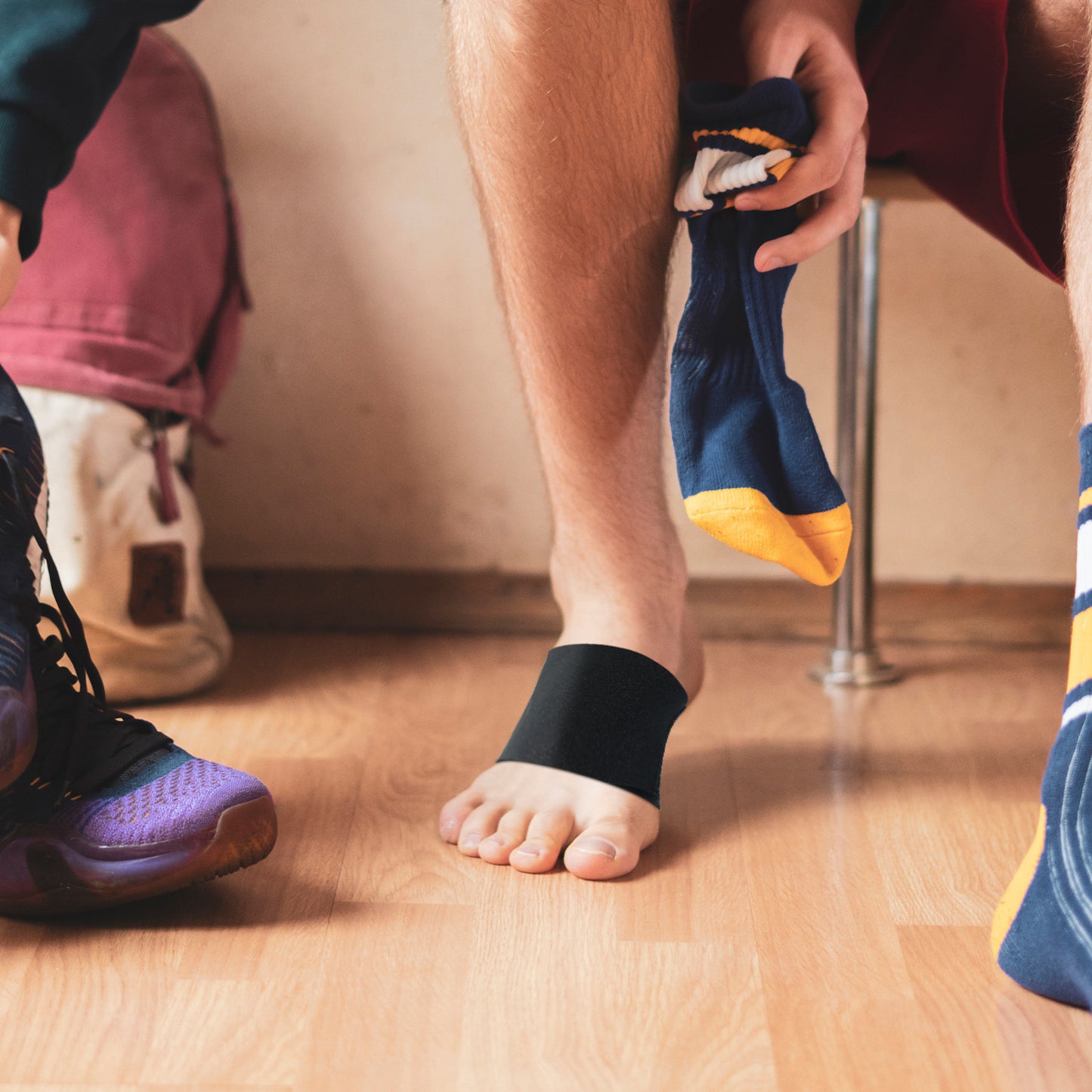 individual wearing a portable foot arch support belt while changing socks in a gym setting